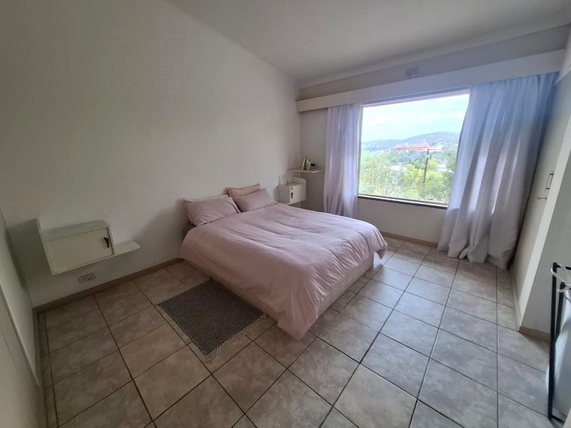 A bright bedroom featuring tiled flooring, built-in wall-mounted shelving, and a large window offering scenic views.