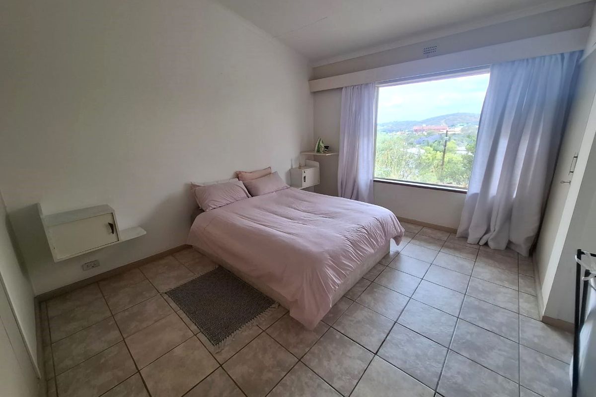 A bright bedroom featuring tiled flooring, built-in wall-mounted shelving, and a large window offering scenic views.