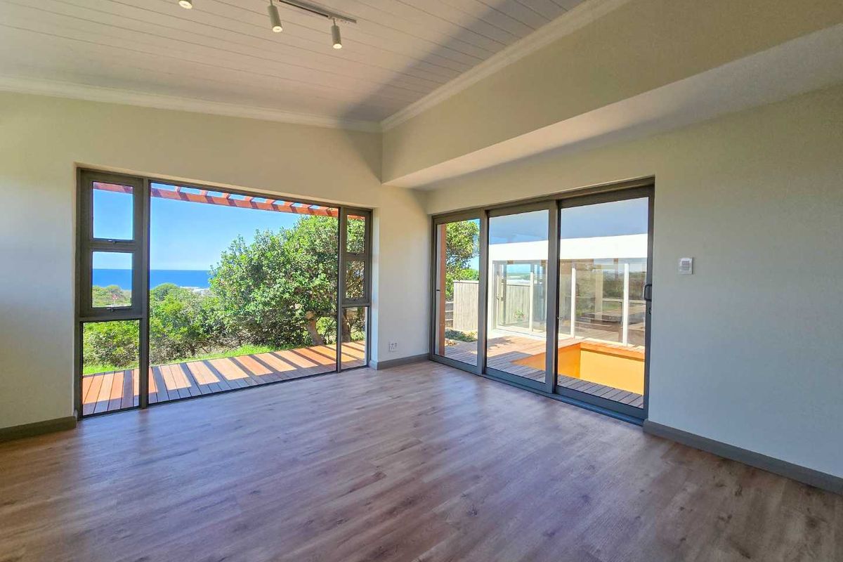 Bright and spacious living area featuring modern wood-look flooring, high ceilings with track lighting, and large sliding glass doors opening to a scenic deck.