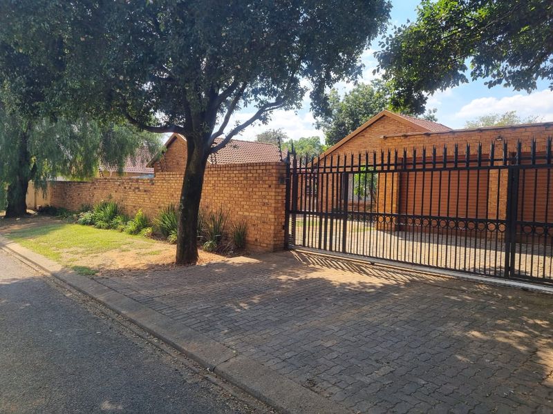Front view of the property featuring a brick boundary wall, secure metal sliding gate, and a paved driveway leading to the house.