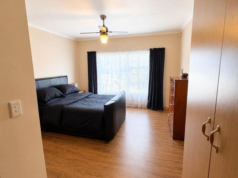 A well-maintained bedroom featuring laminate flooring, a ceiling fan, and built-in cupboards, offering a clean and functional living space.