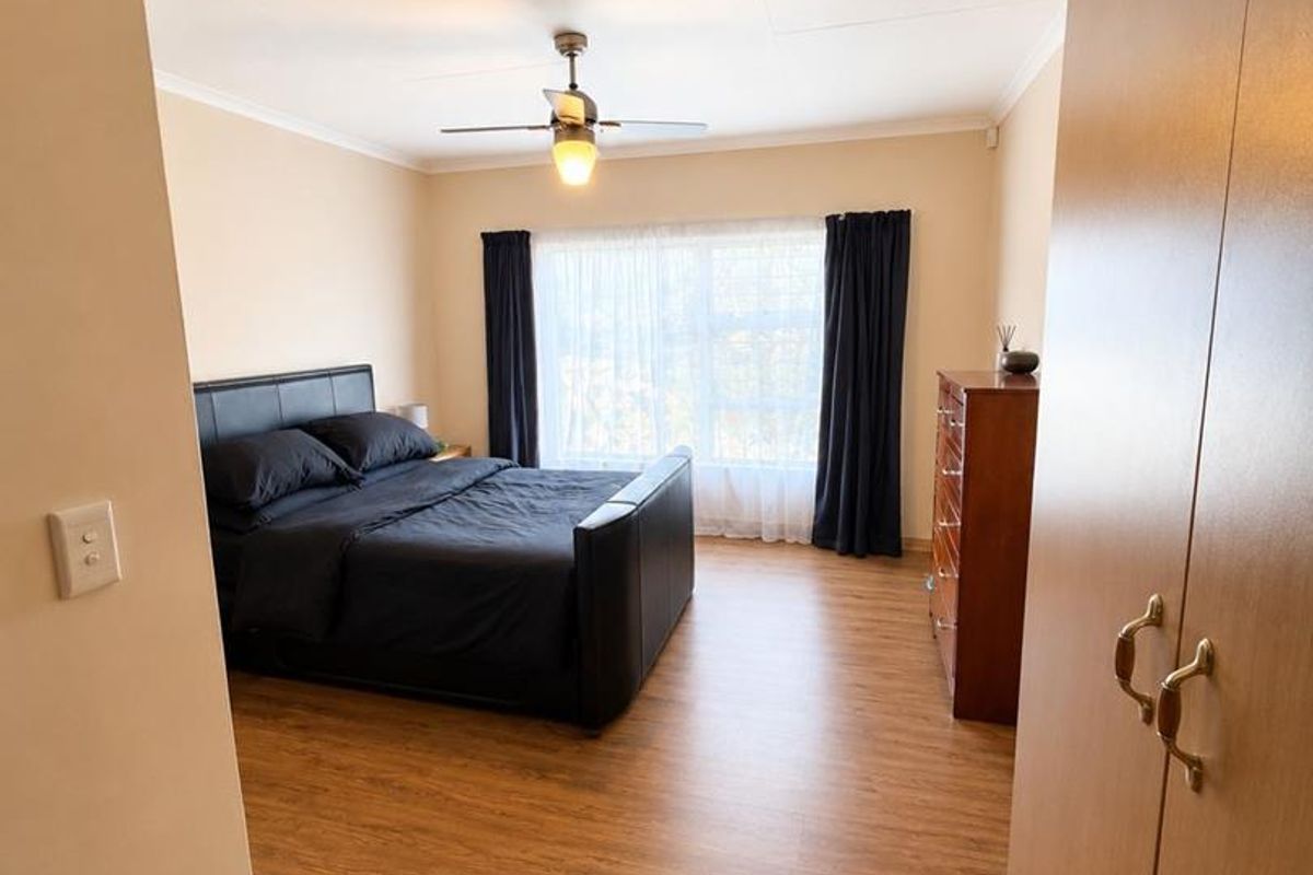A well-maintained bedroom featuring laminate flooring, a ceiling fan, and built-in cupboards, offering a clean and functional living space.