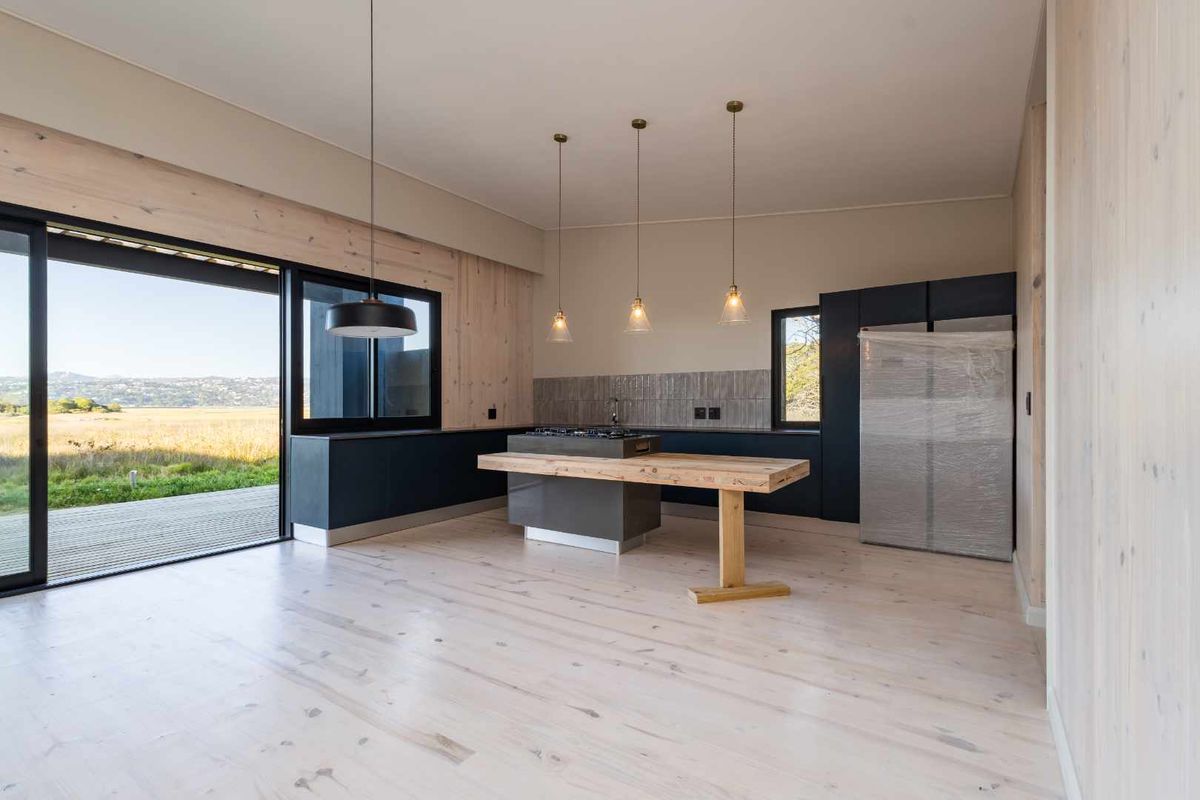Modern open-plan kitchen featuring a central island with integrated hob, sleek cabinetry, and large sliding doors opening to a scenic outdoor view.