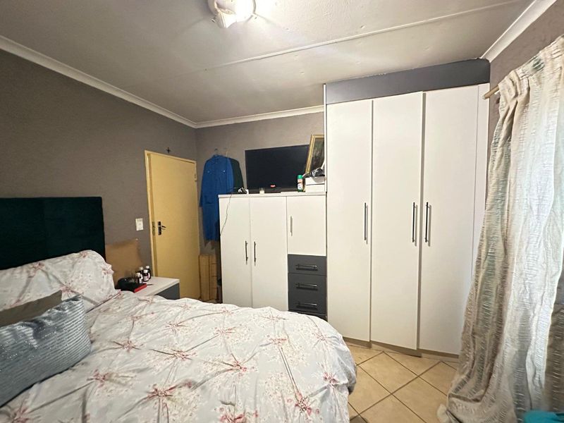 A bedroom featuring built-in cupboards and tiled flooring, showing signs of wear on the ceiling that may require maintenance.