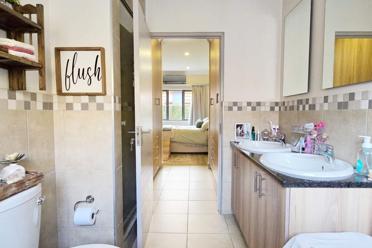 A functional bathroom featuring a double vanity with granite countertops, tiled walls, and a toilet, with a direct view into the adjacent bedroom.
