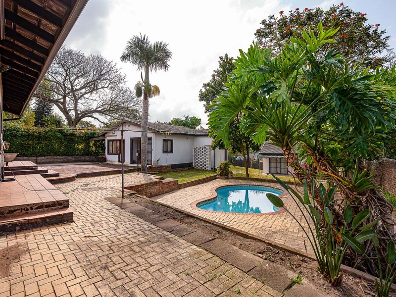 Rear exterior view featuring a paved patio area, a swimming pool, and a covered veranda attached to the main house structure.