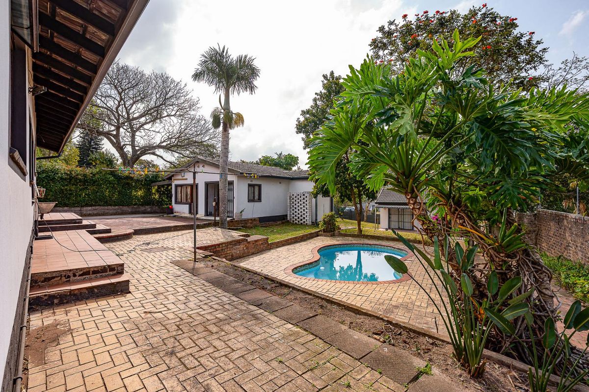 Rear exterior view featuring a paved patio area, a swimming pool, and a covered veranda attached to the main house structure.
