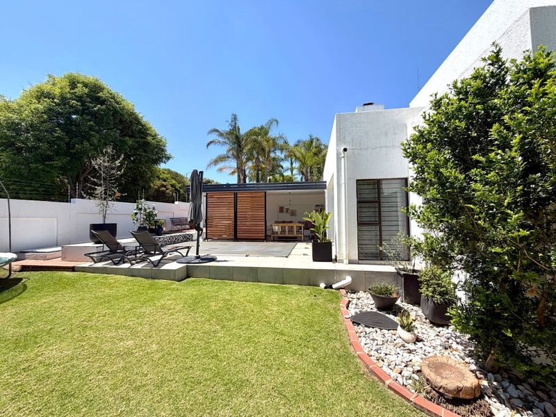 A well-maintained rear garden featuring a swimming pool with a cover, a raised patio area, and established landscaping.