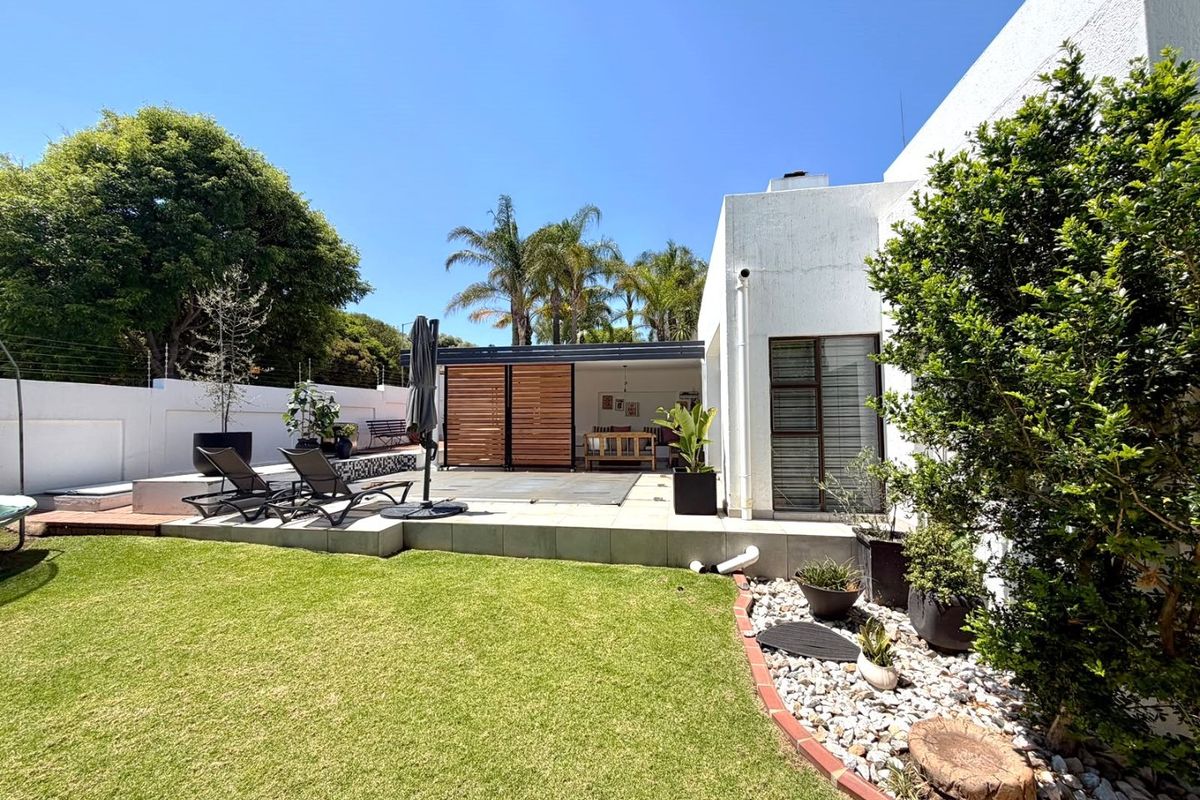 A well-maintained rear garden featuring a swimming pool with a cover, a raised patio area, and established landscaping.