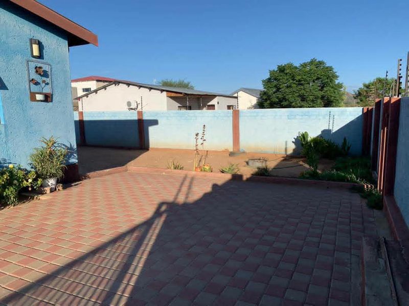 A rear exterior view featuring a paved patio area enclosed by a perimeter wall with electric fencing.
