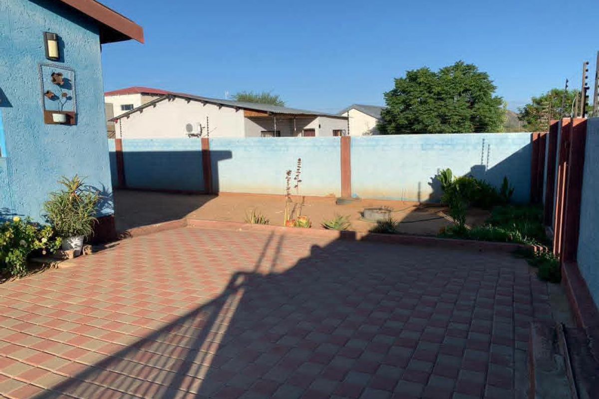A rear exterior view featuring a paved patio area enclosed by a perimeter wall with electric fencing.