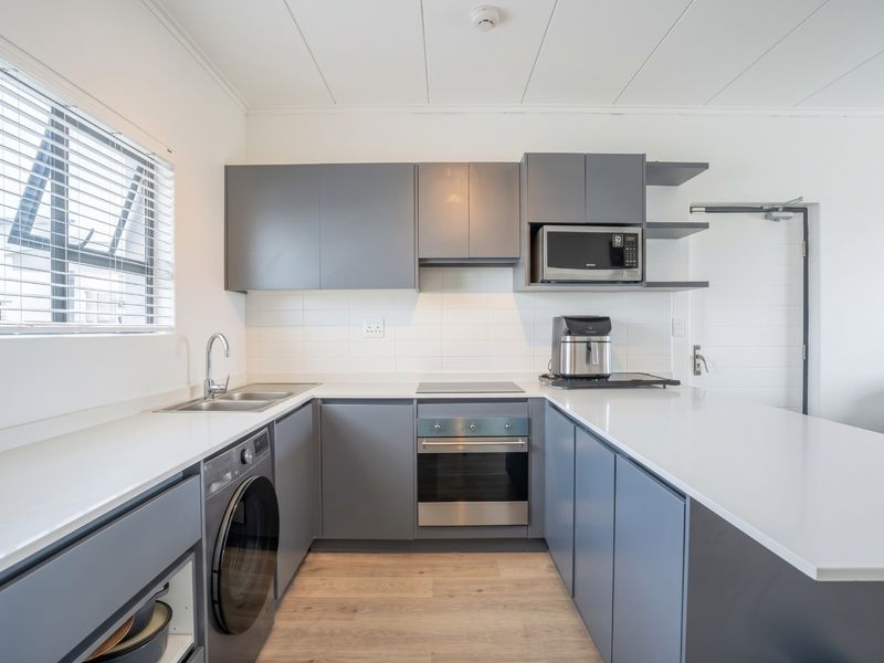 Modern kitchen featuring grey cabinetry, white stone countertops, integrated appliances, and a sleek tiled backsplash, offering a clean and functional culinary space.