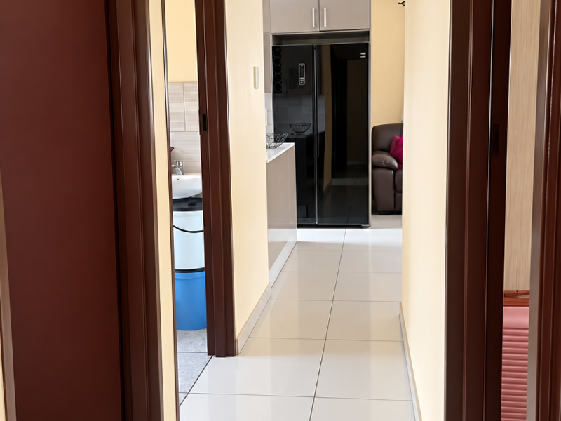 A bright hallway with tiled flooring leading towards a kitchen area, featuring neutral walls and dark wood door frames.