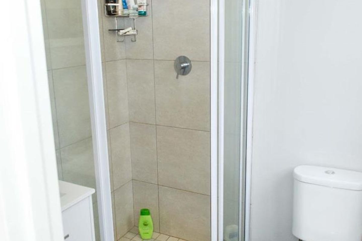 A functional bathroom featuring a corner shower enclosure with tiled walls, a standard toilet, and a vanity cabinet.