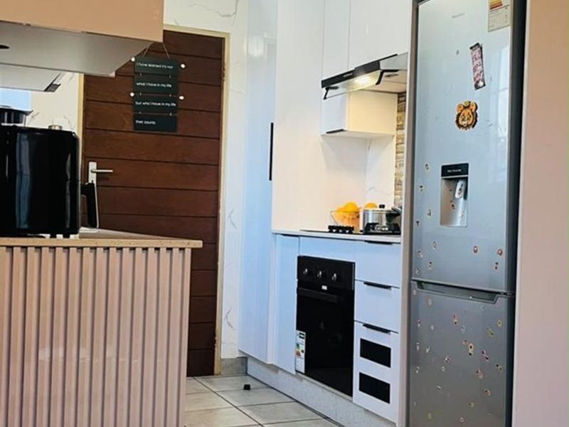 A modern kitchen featuring white cabinetry, built-in oven and hob, extractor fan, and a unique slatted kitchen island with tiled flooring.