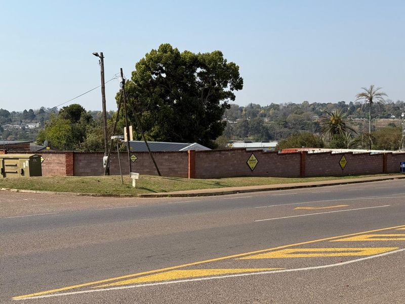 A street-level view of the property boundary featuring a brick perimeter wall, utility infrastructure, and surrounding neighbourhood landscape.