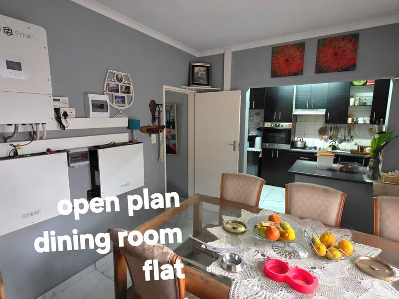 Open plan dining area featuring a modern solar power installation, flowing into a functional kitchen with dark cabinetry and built-in appliances.