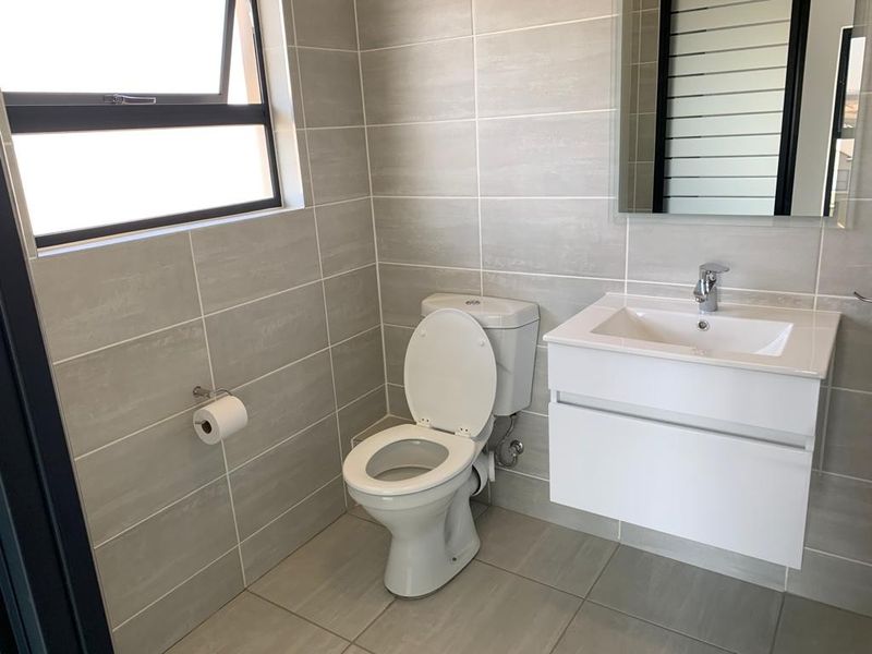 A modern, clean bathroom featuring a wall-mounted vanity with a basin, a toilet, and neutral grey wall and floor tiles.