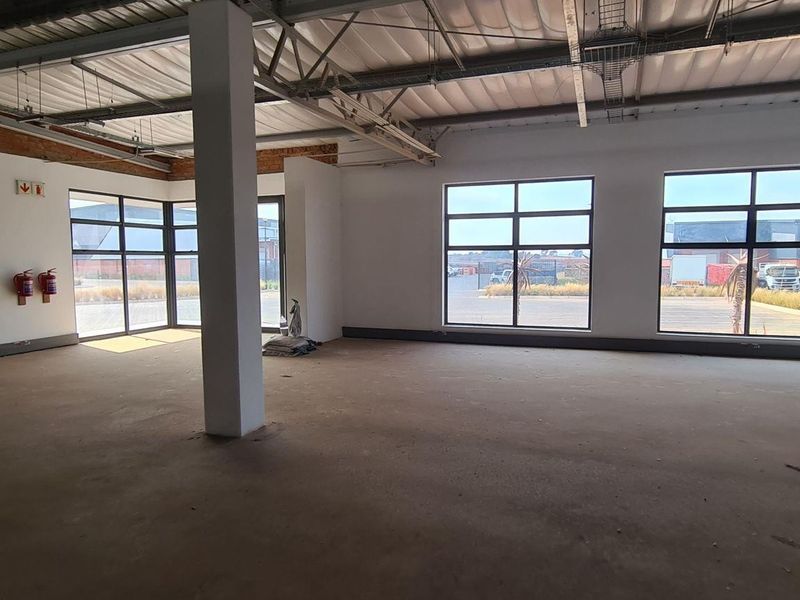Spacious open-plan industrial unit featuring high ceilings with exposed steel trusses, large windows for natural light, and durable concrete flooring.