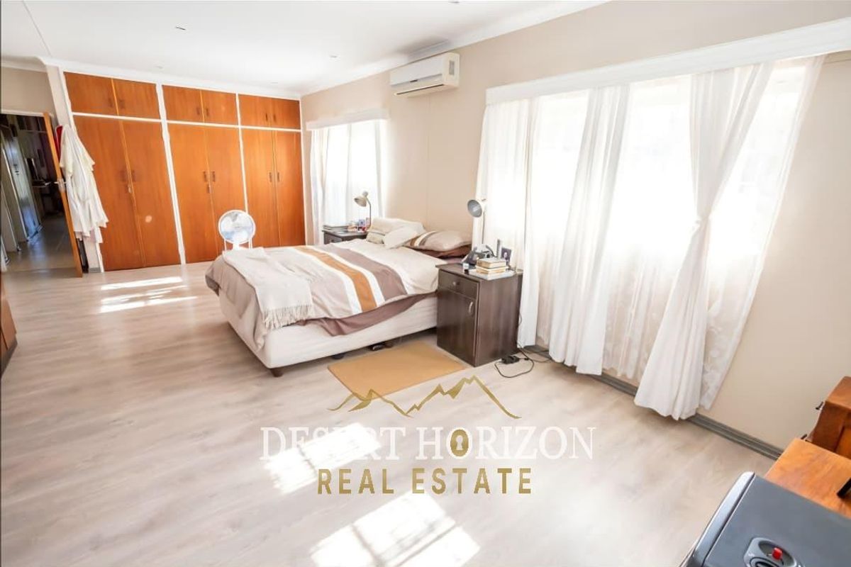 Spacious bedroom featuring light wood-look flooring, built-in wooden cabinetry, and a wall-mounted air conditioning unit.