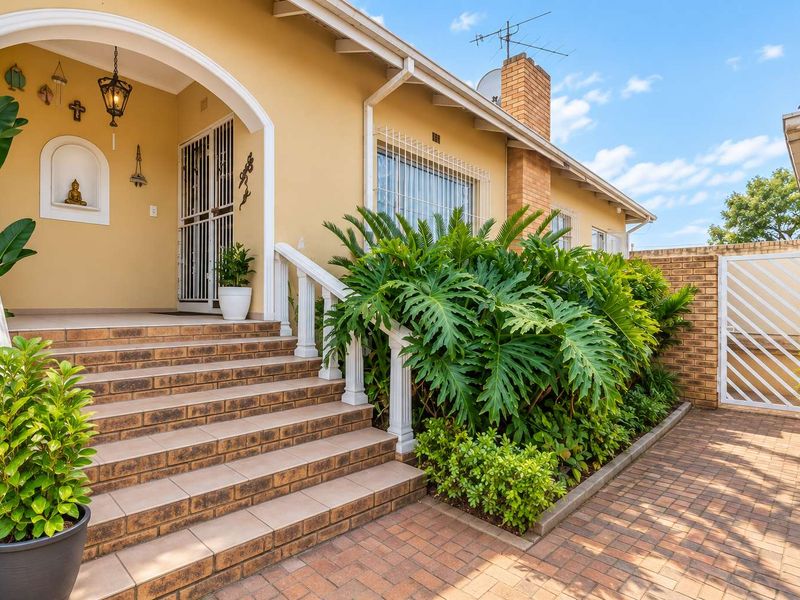 A well-maintained front entrance featuring a tiled staircase, arched porch, and brick facade with established garden landscaping.