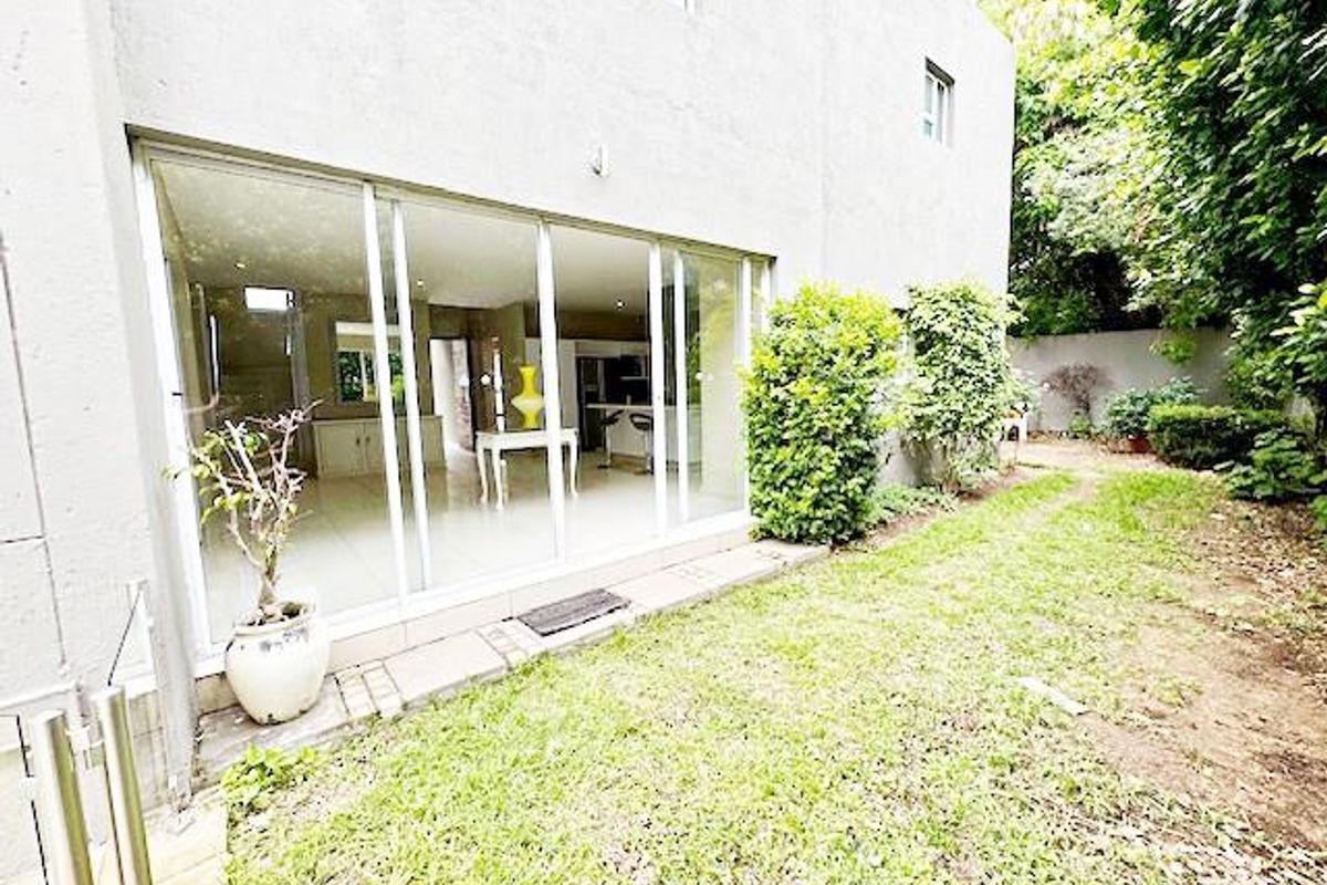 Rear view of the property featuring a lawn, boundary wall, and large sliding glass doors providing access to the interior living space.