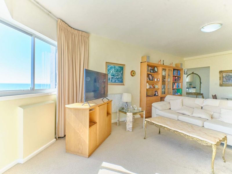 A bright living room featuring carpet flooring, large sliding windows with ocean views, and neutral wall finishes, offering a comfortable and functional living space.