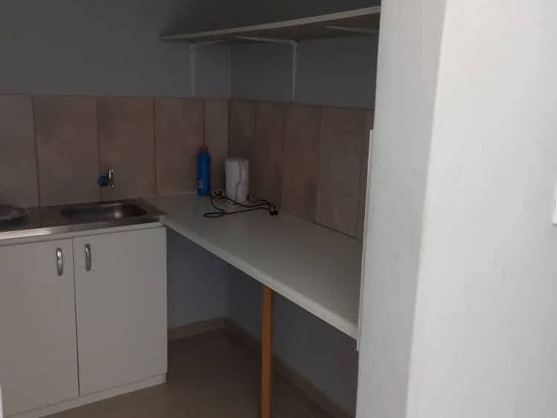 A functional scullery area featuring built-in cabinetry, a stainless steel sink, tiled backsplash, and additional counter space with wall-mounted shelving.