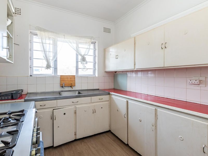 A dated kitchen featuring original cabinetry, a stainless steel sink, and a gas hob, offering significant potential for a modern renovation.