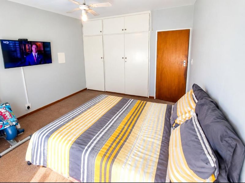 A functional bedroom featuring built-in cupboards, a ceiling fan, and carpeted flooring.