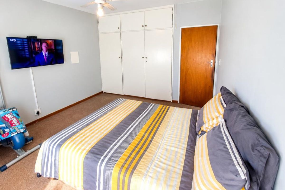 A functional bedroom featuring built-in cupboards, a ceiling fan, and carpeted flooring.