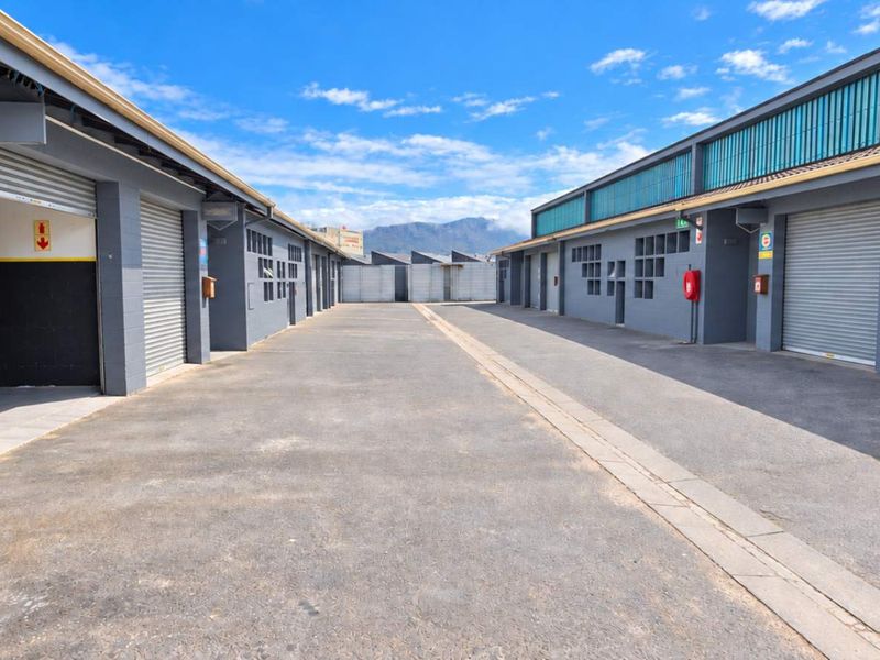A well-maintained industrial complex featuring multiple storage units with roller shutter doors and a central asphalt driveway.