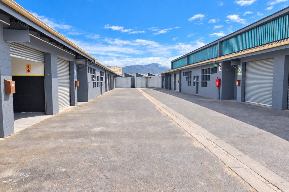 A well-maintained industrial complex featuring multiple storage units with roller shutter doors and a central asphalt driveway.
