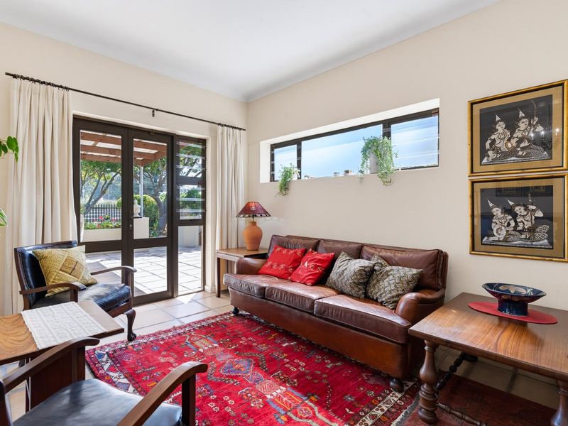 A bright living room featuring tiled flooring, a horizontal clerestory window, and direct access to an outdoor patio through glass-paneled french doors.