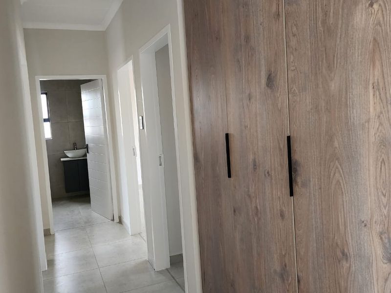 A clean, modern hallway featuring neutral tiled flooring and large built-in wooden cupboards, providing ample storage space and access to adjacent rooms.