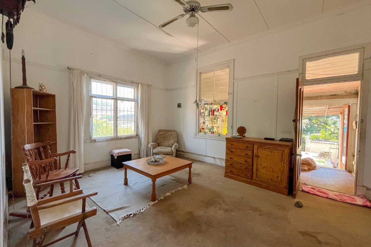 A spacious living room featuring high ceilings, a ceiling fan, and a unique stained glass window detail, offering potential for renovation and modernization.