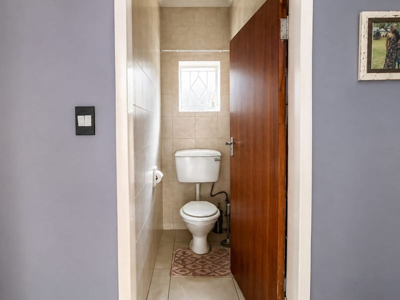 A compact guest bathroom featuring tiled walls, a standard toilet, and a small window, providing a functional and clean utility space.