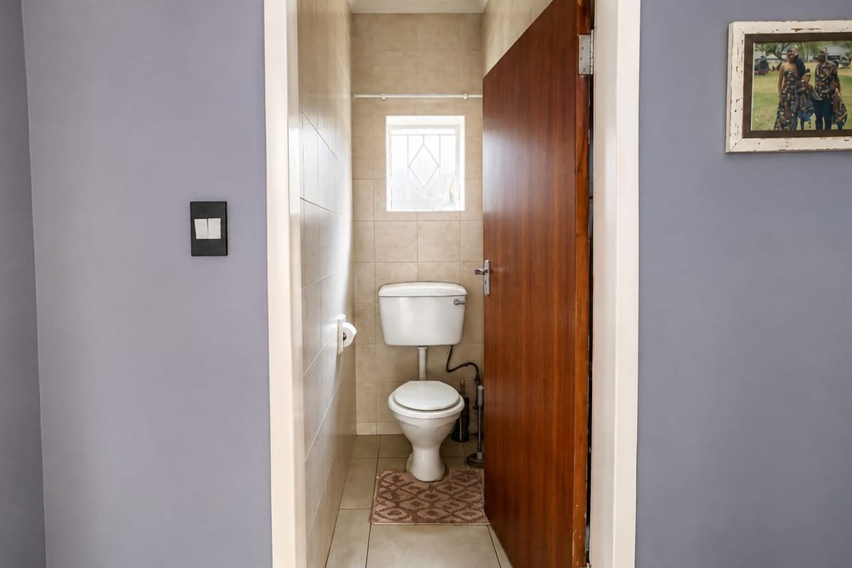 A compact guest bathroom featuring tiled walls, a standard toilet, and a small window, providing a functional and clean utility space.