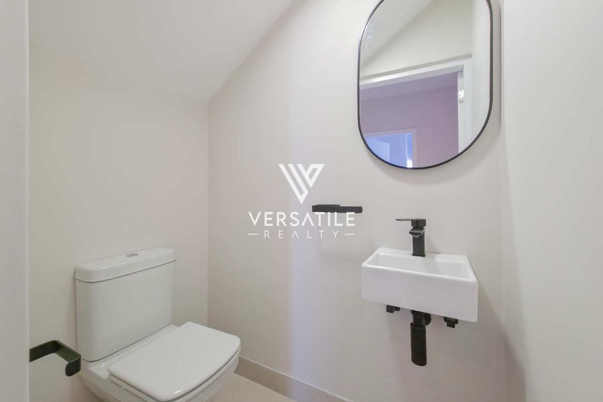 A modern, minimalist powder room featuring a wall-mounted basin with black fixtures, a sleek toilet, and a contemporary wall mirror.