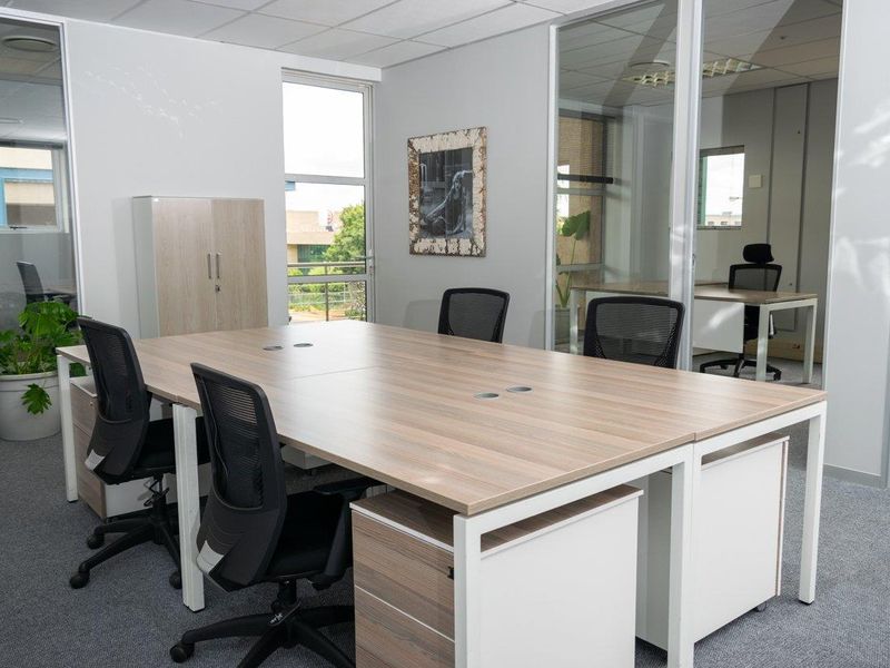 A modern, well-lit office space featuring glass partition walls, suspended ceilings, and carpeted flooring, providing a professional and functional work environment.