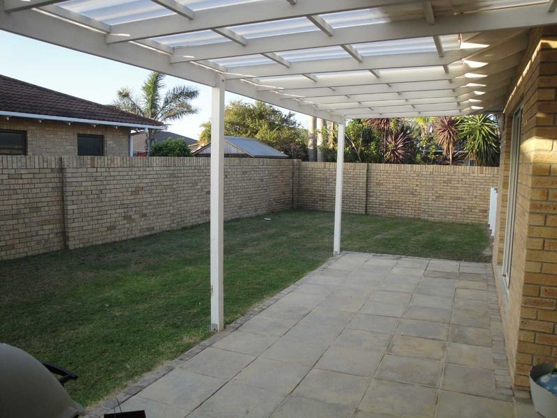 A covered patio area featuring a pergola structure, paved flooring, and a private rear garden enclosed by brick boundary walls.
