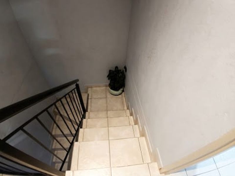 A staircase featuring tiled steps and a black metal handrail, providing access between levels in the townhouse.