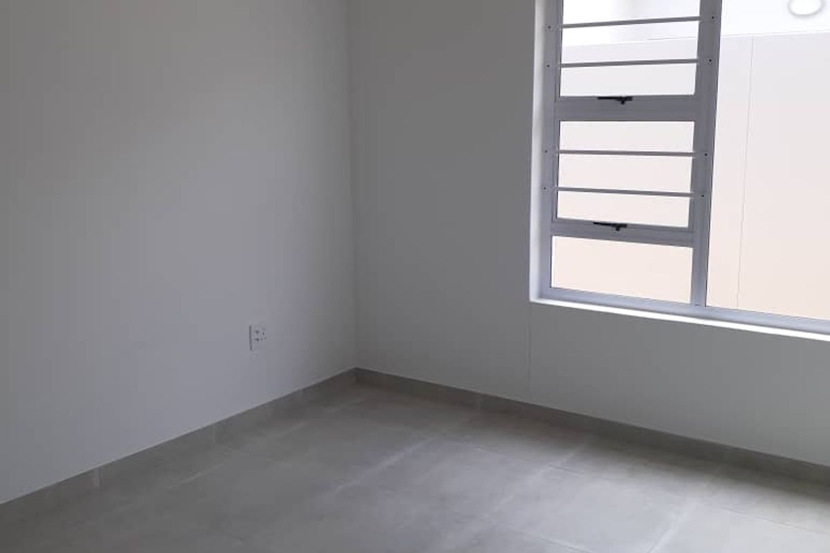 A clean, empty bedroom featuring neutral grey floor tiles, white walls, and a modern aluminium-framed window.