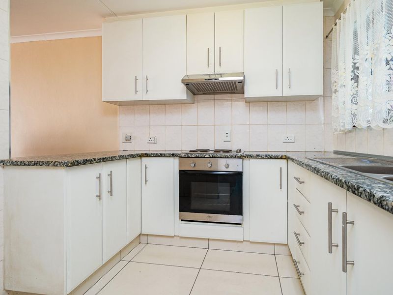 A functional kitchen featuring white cabinetry, granite countertops, built-in oven, hob, extractor fan, and tiled flooring with a double bowl sink.