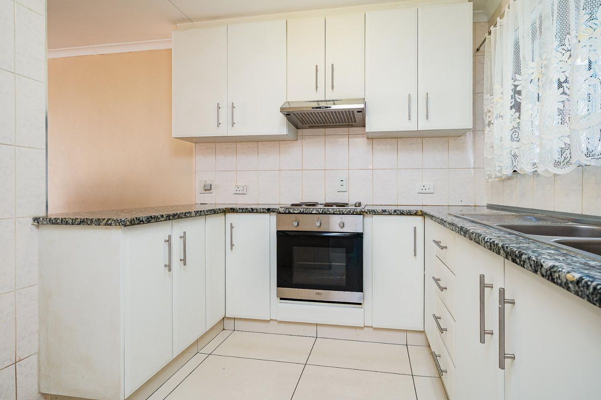 A functional kitchen featuring white cabinetry, granite countertops, built-in oven, hob, extractor fan, and tiled flooring with a double bowl sink.