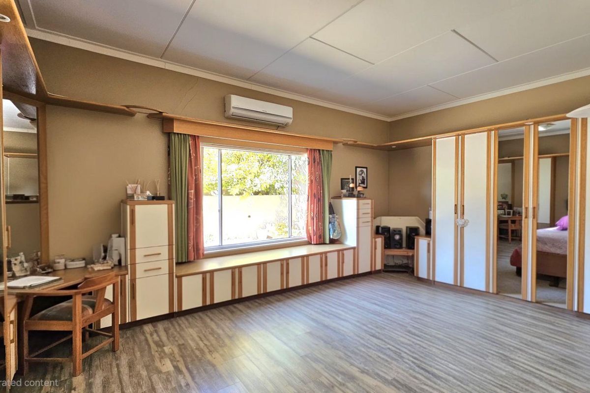 Spacious bedroom featuring extensive built-in cabinetry, a window seat, split-system air conditioning, and durable laminate flooring.