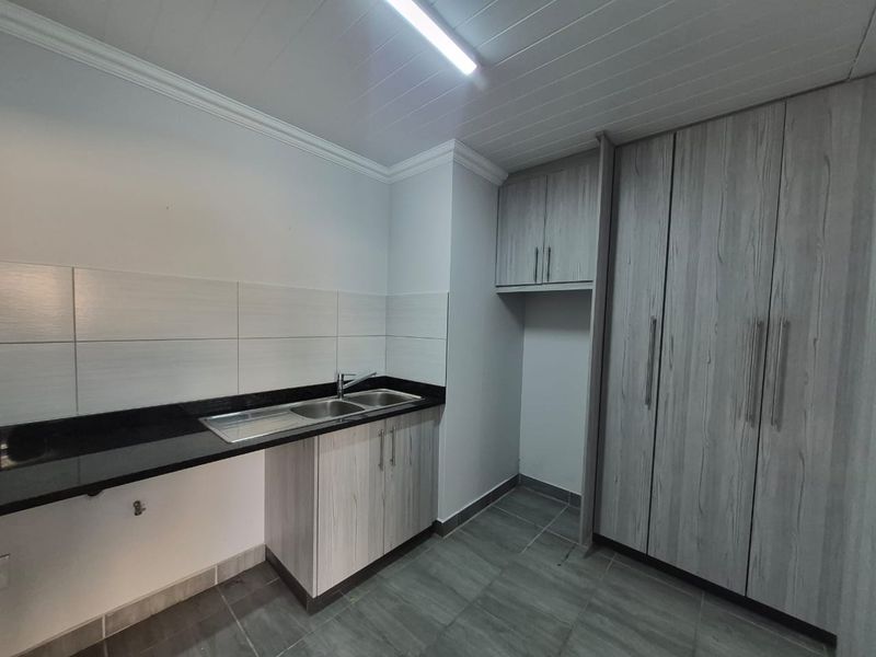 A clean and functional laundry area featuring built-in cabinetry, a stainless steel sink with granite countertop, and modern tiled finishes.