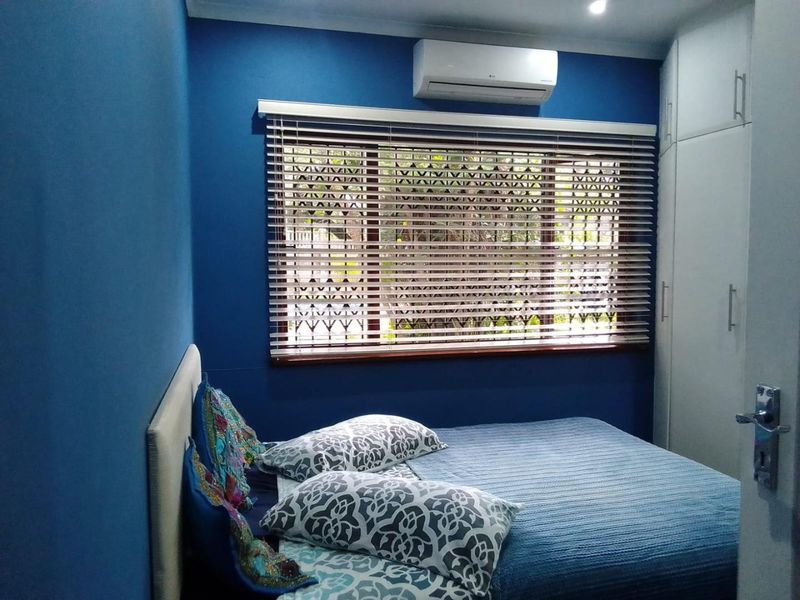 A well-maintained bedroom featuring built-in cupboards, a wall-mounted air conditioning unit, and venetian blinds.