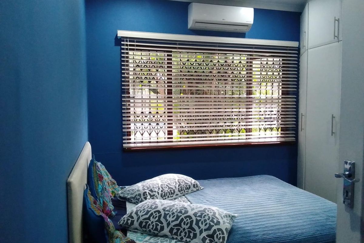 A well-maintained bedroom featuring built-in cupboards, a wall-mounted air conditioning unit, and venetian blinds.