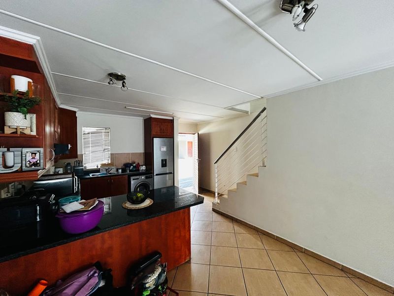 Open plan kitchen featuring granite countertops and wooden cabinetry, seamlessly flowing into the living area with tiled flooring and a staircase.